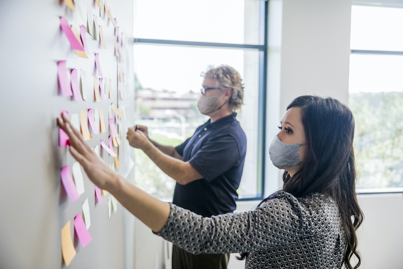 Two people leading a brainstorming session by putting post it notes on the wall