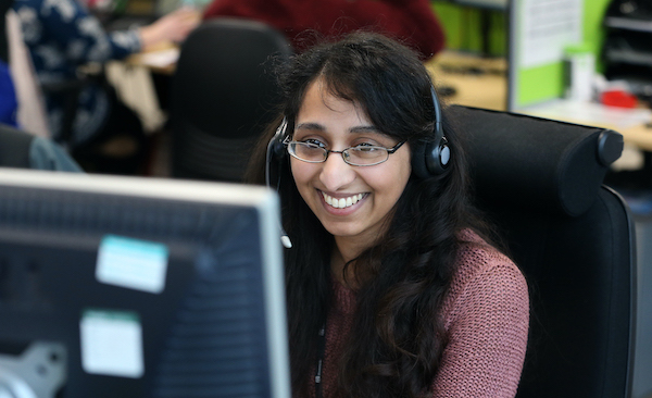 Woman wearing headset, smiling while looking at computer