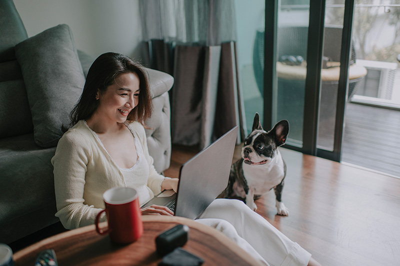 Woman working on computer while sitting next to a dog