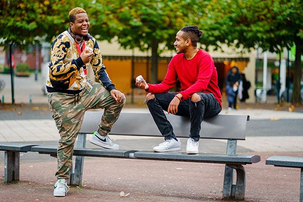 Two young men smiling and laughing on a park bench.