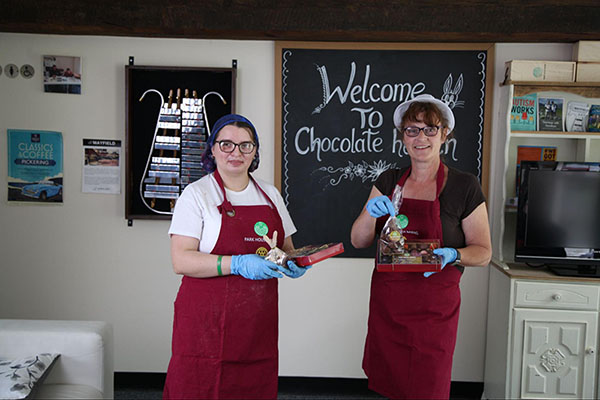 Two women in aprons holding handmade chocolate.
