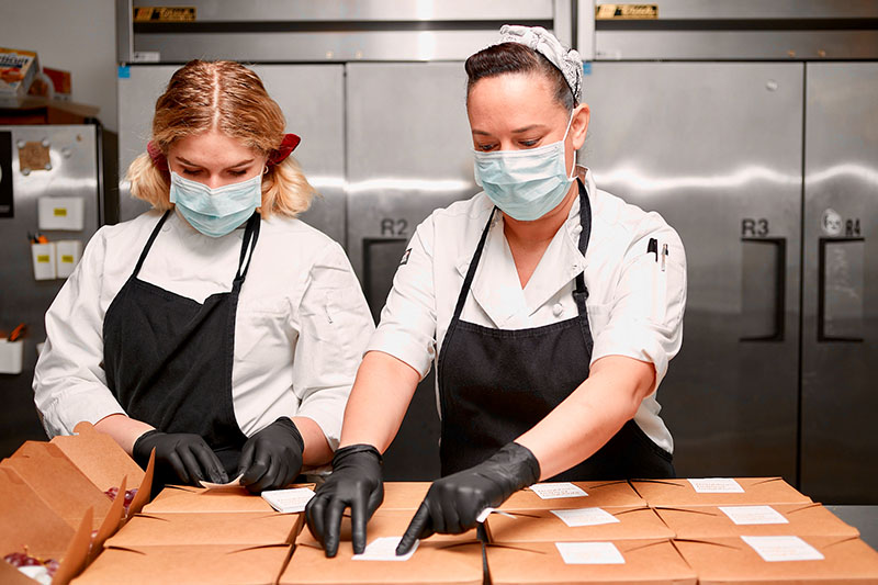 Two people boxing up meals in a kitchen