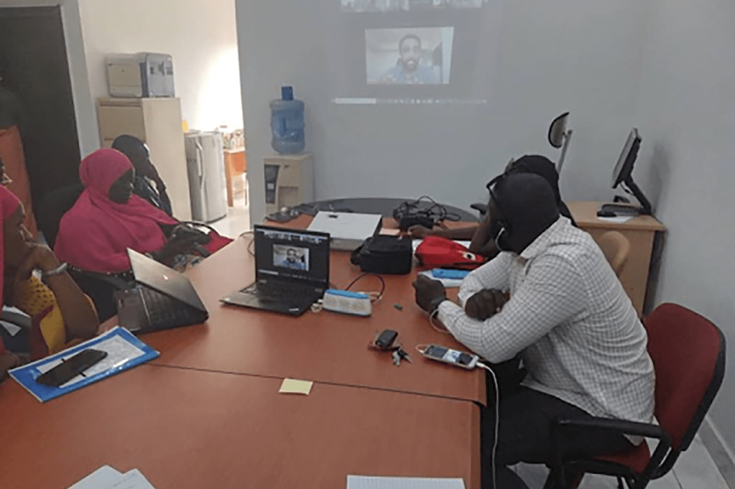 Men and women sitting at a table looking at a video call screen