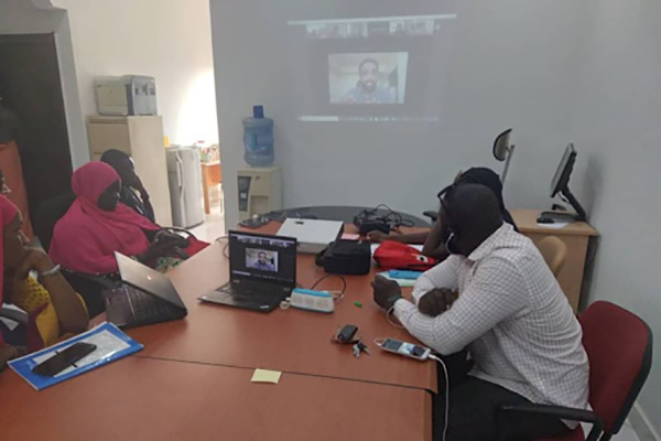 Men and women sitting at a table looking at a video call screen