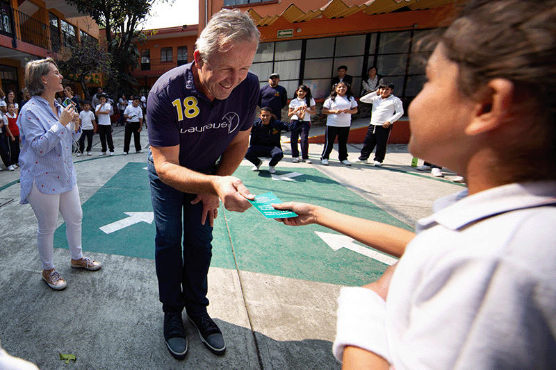 A child is handing a piece of paper to Sean Fitzpatrick as he visits the Laureus Sport for Good program in Mexico City